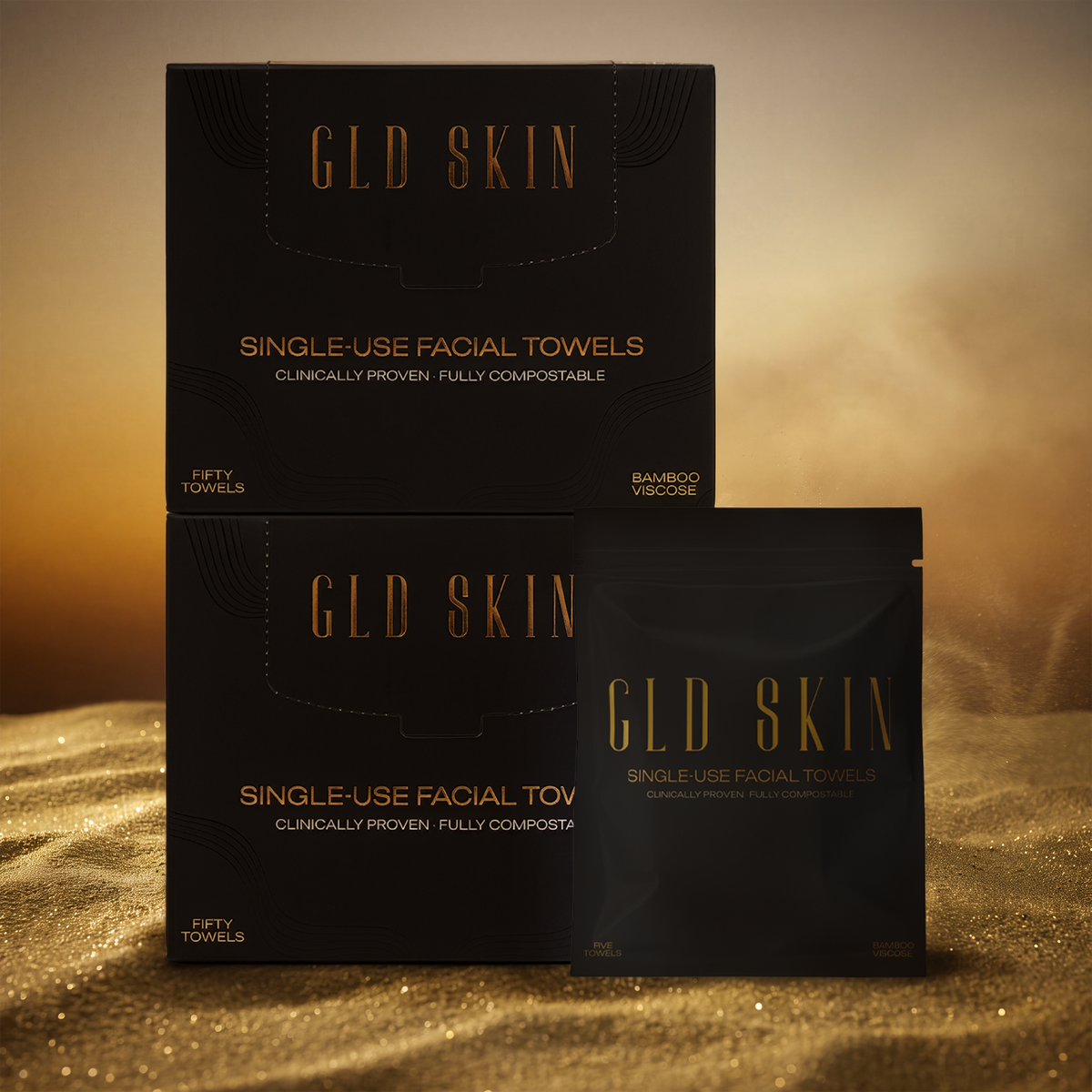 GLD SKIN single-use facial towels packaging, including a larger box and a single sachet, in black with gold lettering, set against a warm golden background resembling sand.
