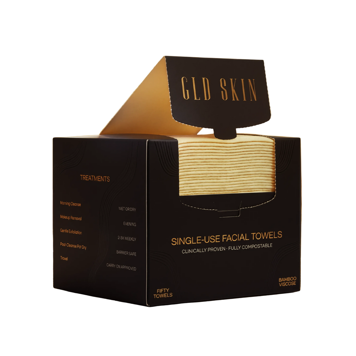 A black GLD SKIN single-use facial towel box with a hinged lid, shown on a warm golden surface. The front window reveals folded beige facial towels inside.