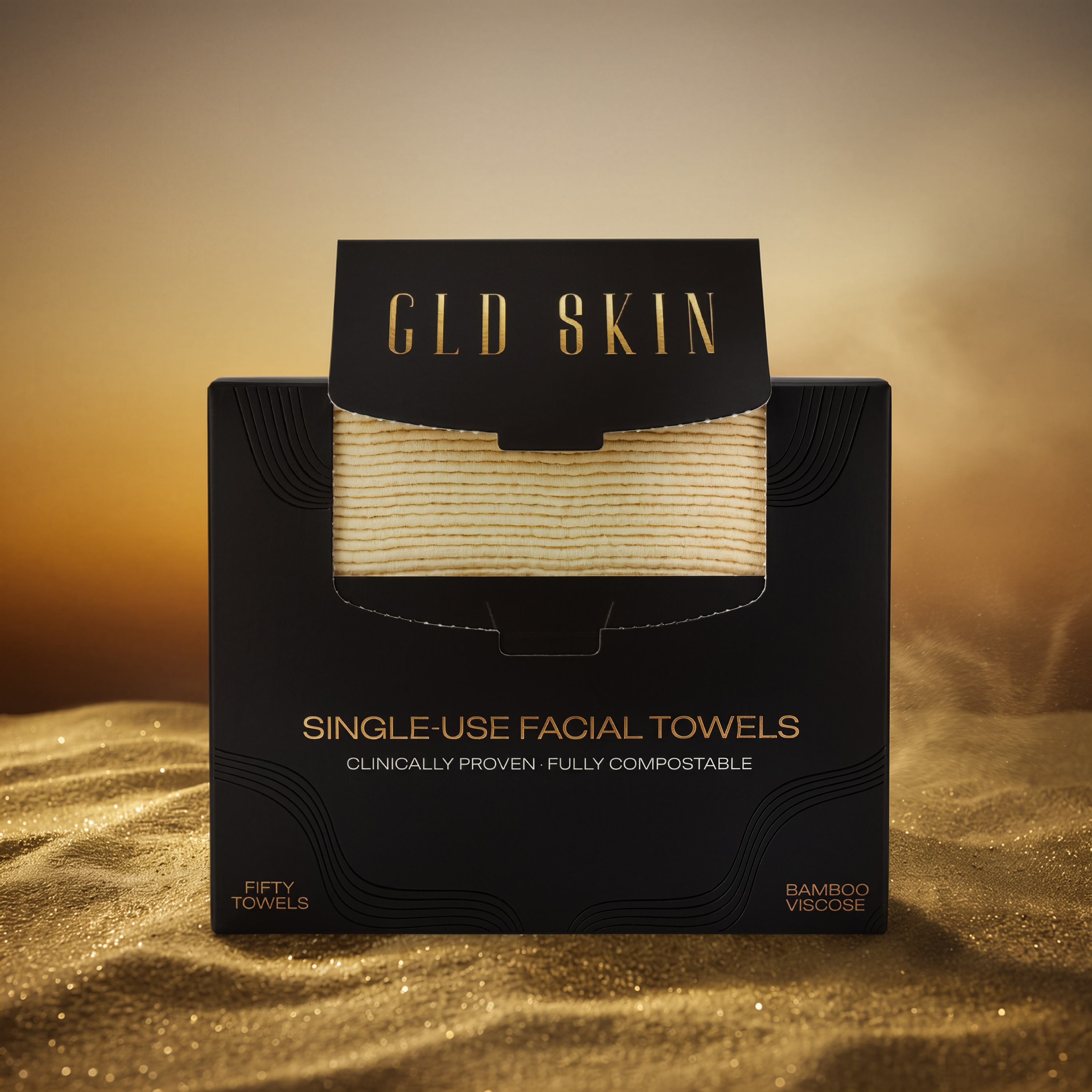 A black retail box for GLD Skin single-use facial towels, with a clear window showing folded beige towels inside. The box has gold text and is photographed on a warm golden surface with a matching gradient background.
