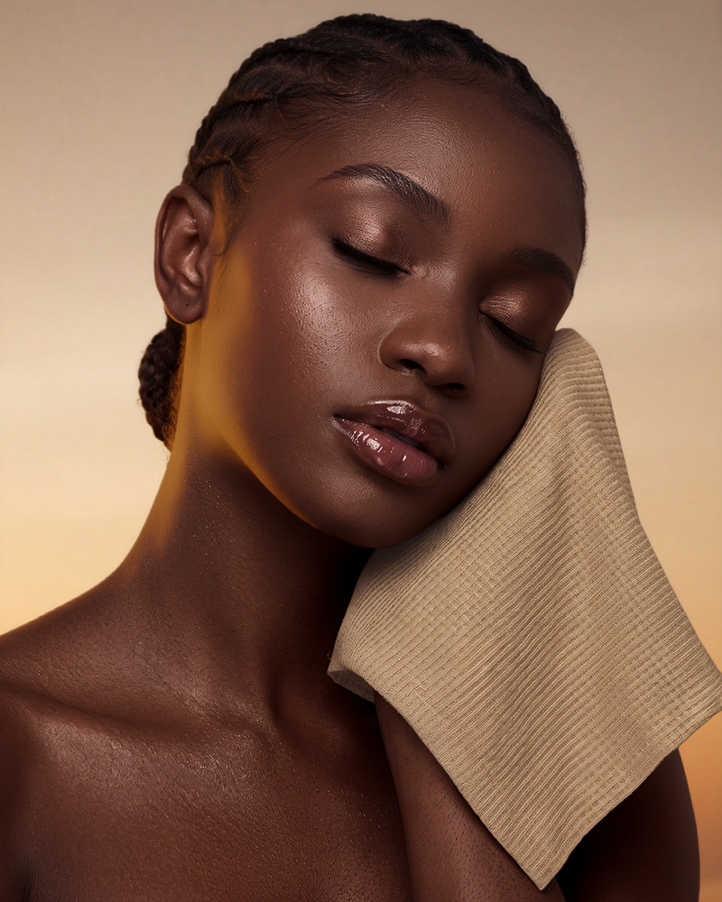 A close-up portrait of a woman with closed eyes resting her head on a beige textured cloth, wearing a nude lip gloss. The brand name 'GLD SKIN' is printed in the top right corner against a warm beige background.